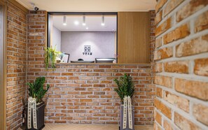 A room with brick walls, a wooden reception desk, and two potted plants. - Incheon Juan Youth Hotel (Incheon)