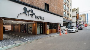 Et hotel med en moderne facade, en overdækket indgang og en parkeringsplads med biler og kegler.