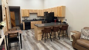 A modern kitchen with wooden cabinets, a black refrigerator, and a bar area with stools.