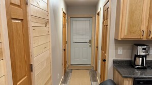 A narrow hallway with wooden paneling on the walls, a door at the end, and a kitchen area with a coffee maker and dishwasher.