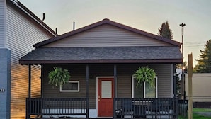 A two-story house with a red door, a covered porch with black railings, and two potted plants on either side.