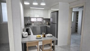A modern kitchen with grey cabinets, a stainless steel refrigerator, a coffee maker, and a dining area with two chairs and a table set with plates and a banana. - Bright & Quiet Easily access to seoul– Monthly Stay (30+ Nights) (Yangju-si)