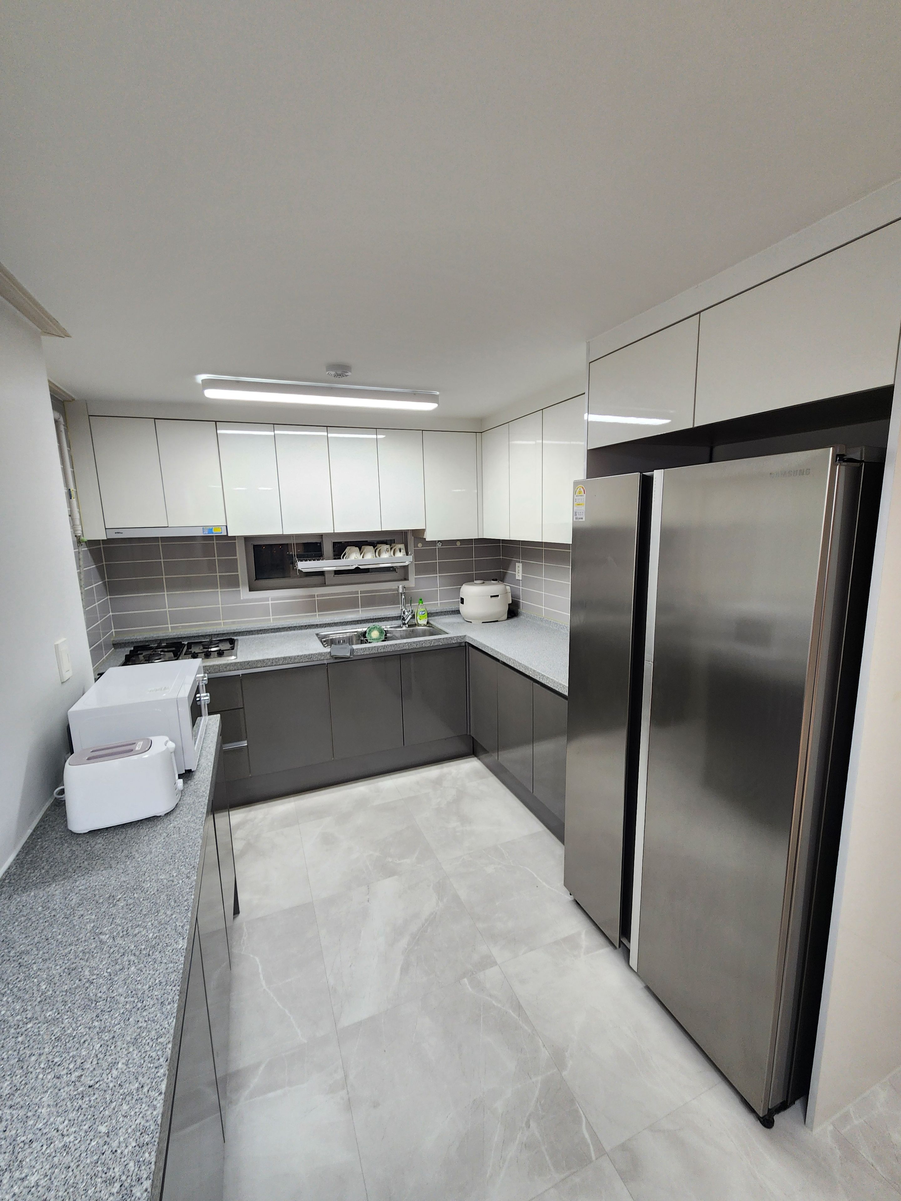 Cozinha moderna com eletrodomésticos de aço inoxidável, painel de backsplash em azulejos cinzas e armários brancos.