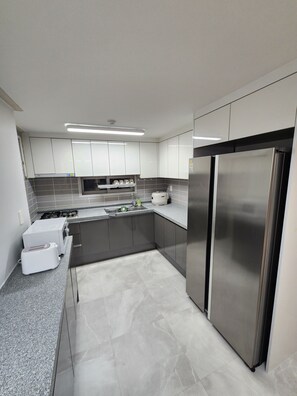 Cozinha moderna com eletrodomésticos de aço inoxidável, painel de backsplash em azulejos cinzas e armários brancos.