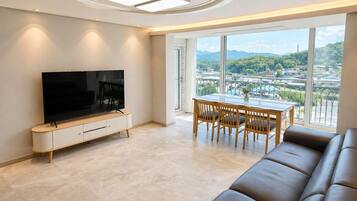 Uma sala de estar moderna com televisão de tela plana, mesa de jantar com cadeiras, sofá de couro e uma grande janela com vista para a cidade.