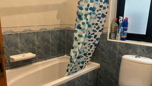 A bathroom with a bathtub, a toilet, and a window with cleaning supplies on the windowsill. - Spacious Room & Shared Bath in Valletta (Ħamrun)