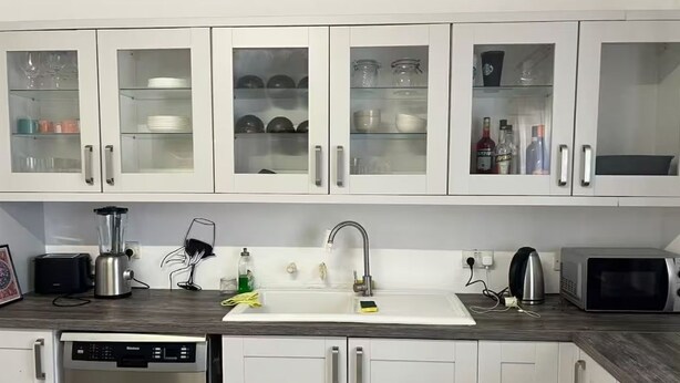 A modern kitchen with white cabinets, a built-in dishwasher, a sink with a faucet, a toaster, a kettle, and a microwave. - Spacious Room & Shared Bath in Valletta (Ħamrun)