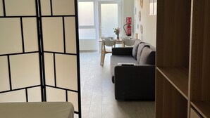 A modern hotel room with a bed, a sofa, a wooden wardrobe, and a dining area with a table and chairs.