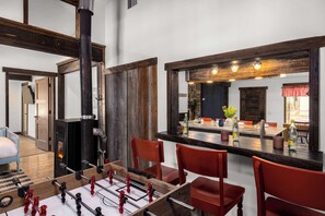 A cozy room with a foosball table, a fireplace, and a dining area with red chairs and a bar counter.