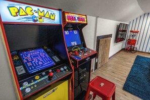 Two arcade machines, one labeled 'PAC-MAN' and the other 'NBA JAM', in a room with wooden flooring and a blue rug.