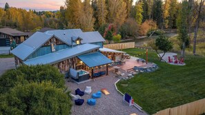 A lodge with a large deck, outdoor seating, and a hot tub. - River's Ranch - Riverfront with Hot Tub & Theater (Kalispell)