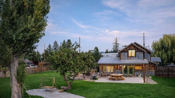 A rustic cabin with a large deck, outdoor seating, and a well-maintained yard. - River's Ranch - Riverfront with Hot Tub & Theater (Kalispell)