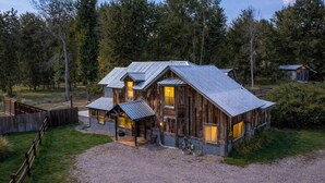 A rustic cabin with a metal roof, wooden walls, and a gravel driveway. - River's Ranch - Riverfront with Hot Tub & Theater (Kalispell)
