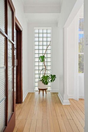 A hallway with wooden flooring, white walls, and a large window with blinds. - Beauty at the Papilo (Holdfast Bay)