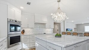 Een moderne keuken met witte kasten, een groot eiland, roestvrijstalen apparatuur en een bijzondere kroonluchter.