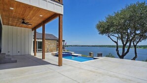 Een modern huis met een overdekt terras, een zwembad en uitzicht op een meer.