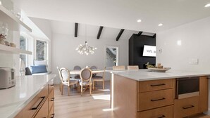Ett modernt kök med en central köksö, träskåp och en matplats med stolar.