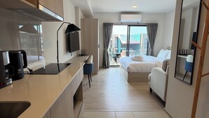 Moderni hotellihuone, jossa on pieni keittiönurkkaus, sänky, oleskelualue ja suuri peili.