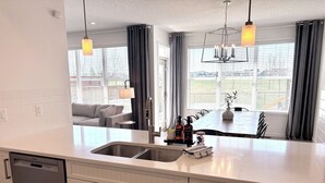A modern kitchen with a dishwasher, a sink, and a dining area with a table and chairs. - Spacious 5BR Retreat w/ Hot Tub, Fire Pit, Gym & Movie Room (Calgary)