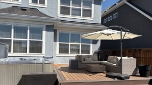 A backyard with a hot tub, outdoor seating, and a pergola with an umbrella. - Spacious 5BR Retreat w/ Hot Tub, Fire Pit, Gym & Movie Room (Calgary)