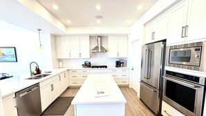 A modern kitchen with white cabinetry, stainless steel appliances, and a central island. - Spacious 5BR Retreat w/ Hot Tub, Fire Pit, Gym & Movie Room (Calgary)
