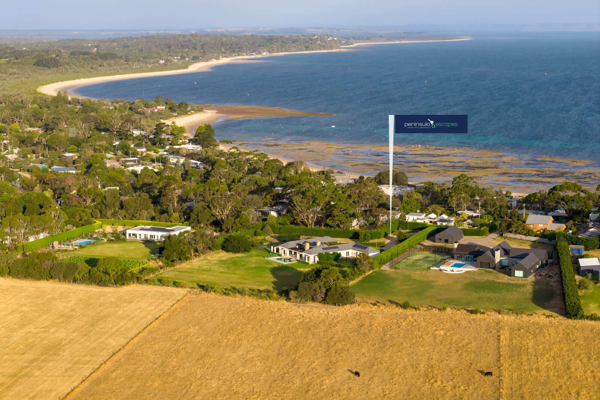An aerial view of a coastal residential area with houses, a beach, and a large body of water.