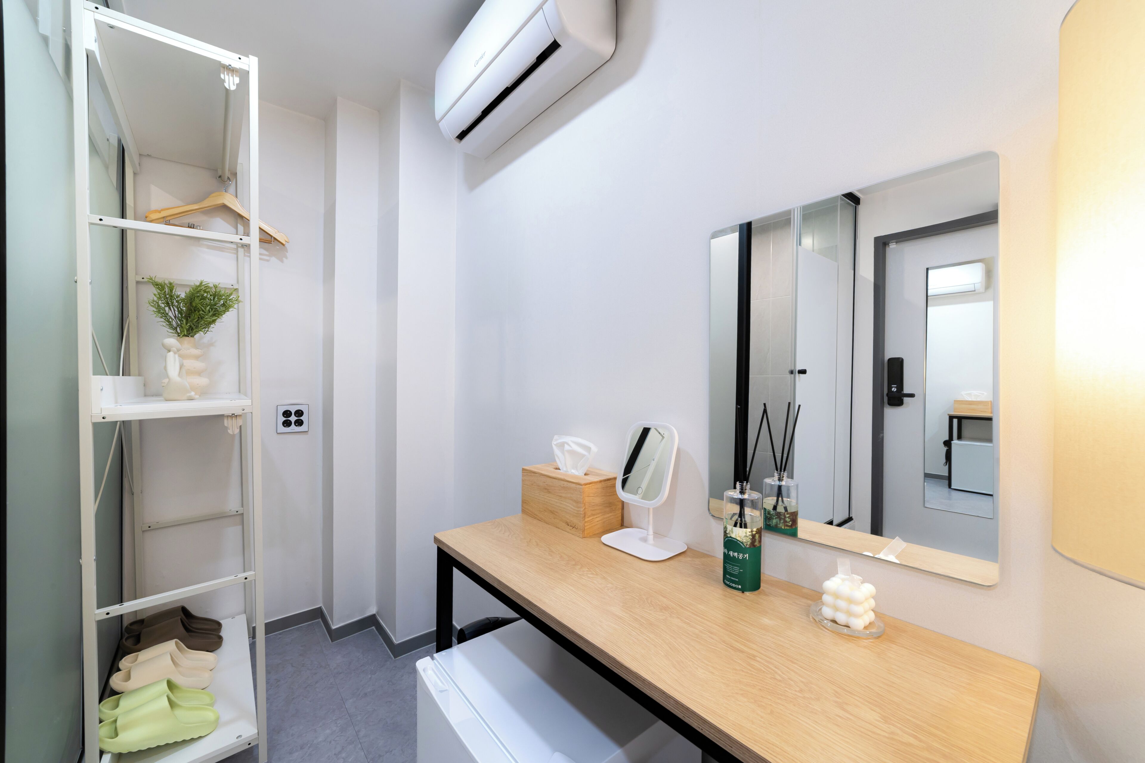 A modern bathroom with a wooden vanity, a mirror, a towel rack, and a shelf with slippers.