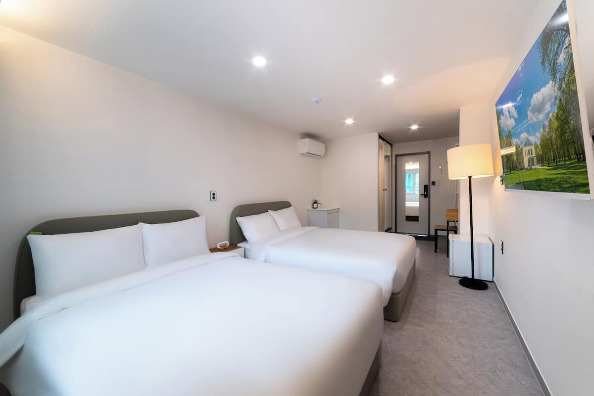 Una habitación de hotel con dos camas, un escritorio, una lámpara y un cuadro en la pared.