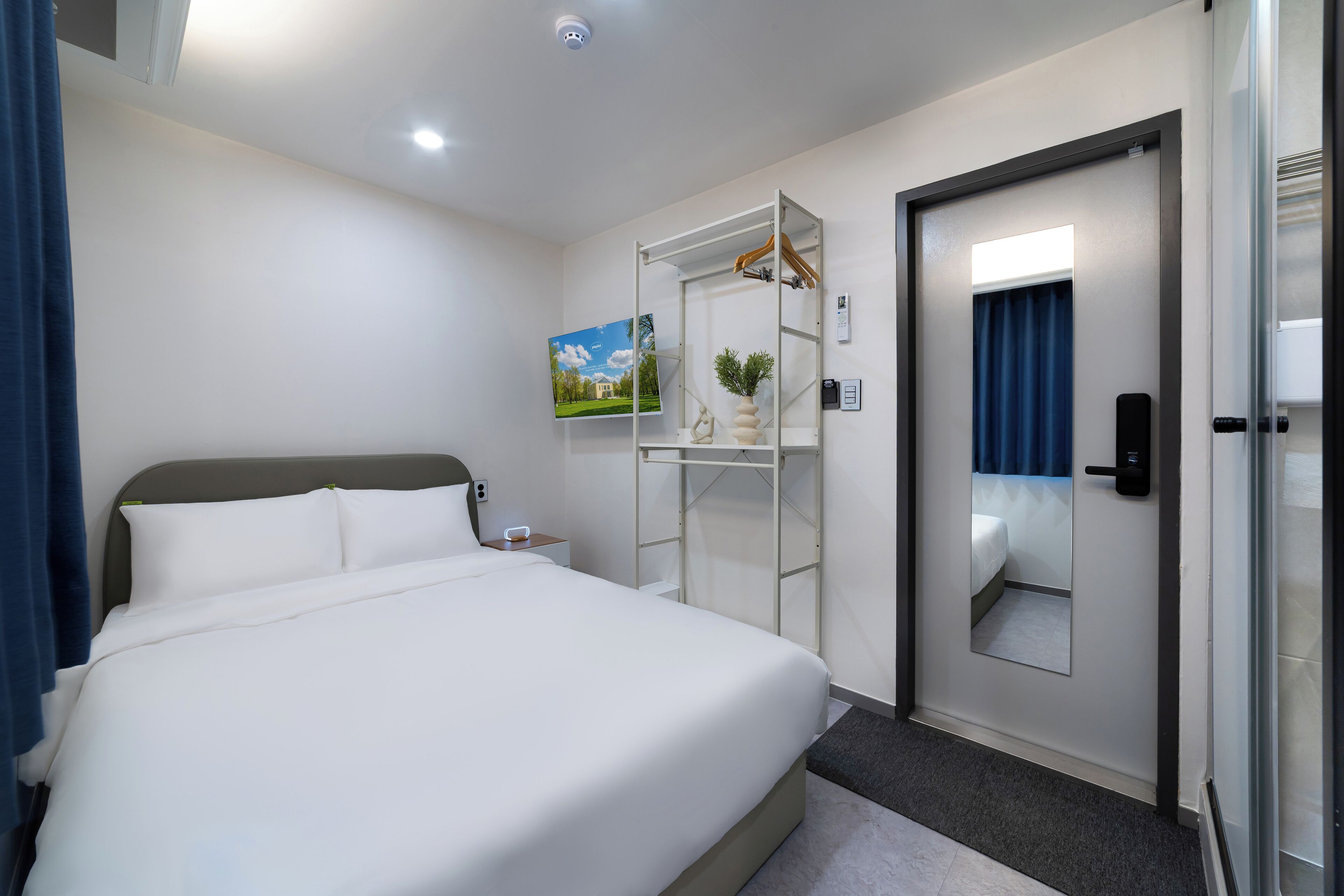 A hotel room with a large bed, a wardrobe with a mirror, a small bedside table, and a painting on the wall.