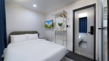 A hotel room with a large bed, a wardrobe with a mirror, a small bedside table, and a painting on the wall.
