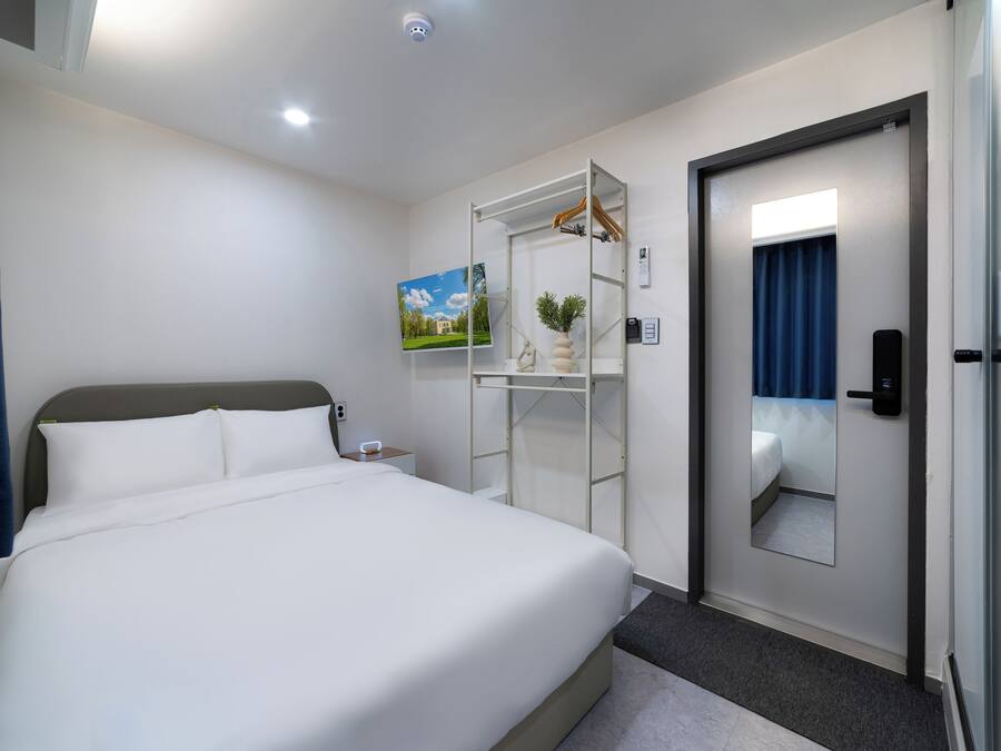 A hotel room with a large bed, a wardrobe with a mirror, a small bedside table, and a painting on the wall.