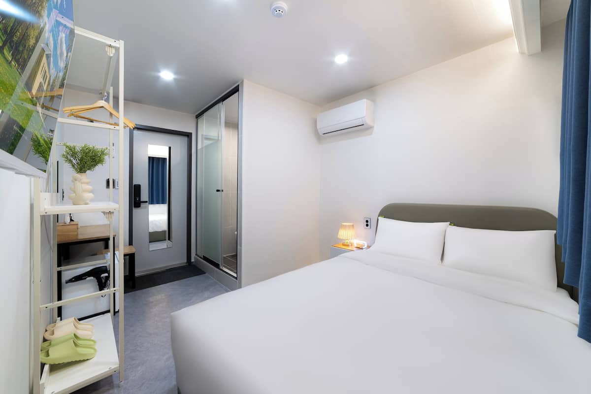 Una habitación de hotel con una cama, un armario, un espejo, una puerta y un equipo de aire acondicionado.