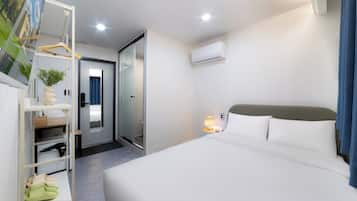 A hotel room with a bed, a wardrobe, a mirror, a door, and an air conditioning unit.