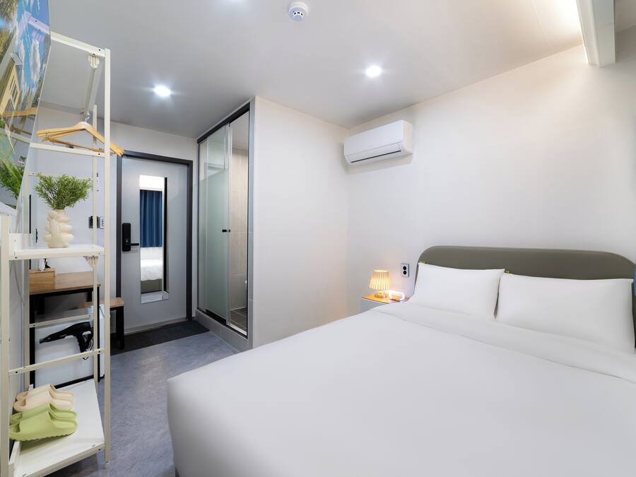 A hotel room with a bed, a wardrobe, a mirror, a door, and an air conditioning unit.