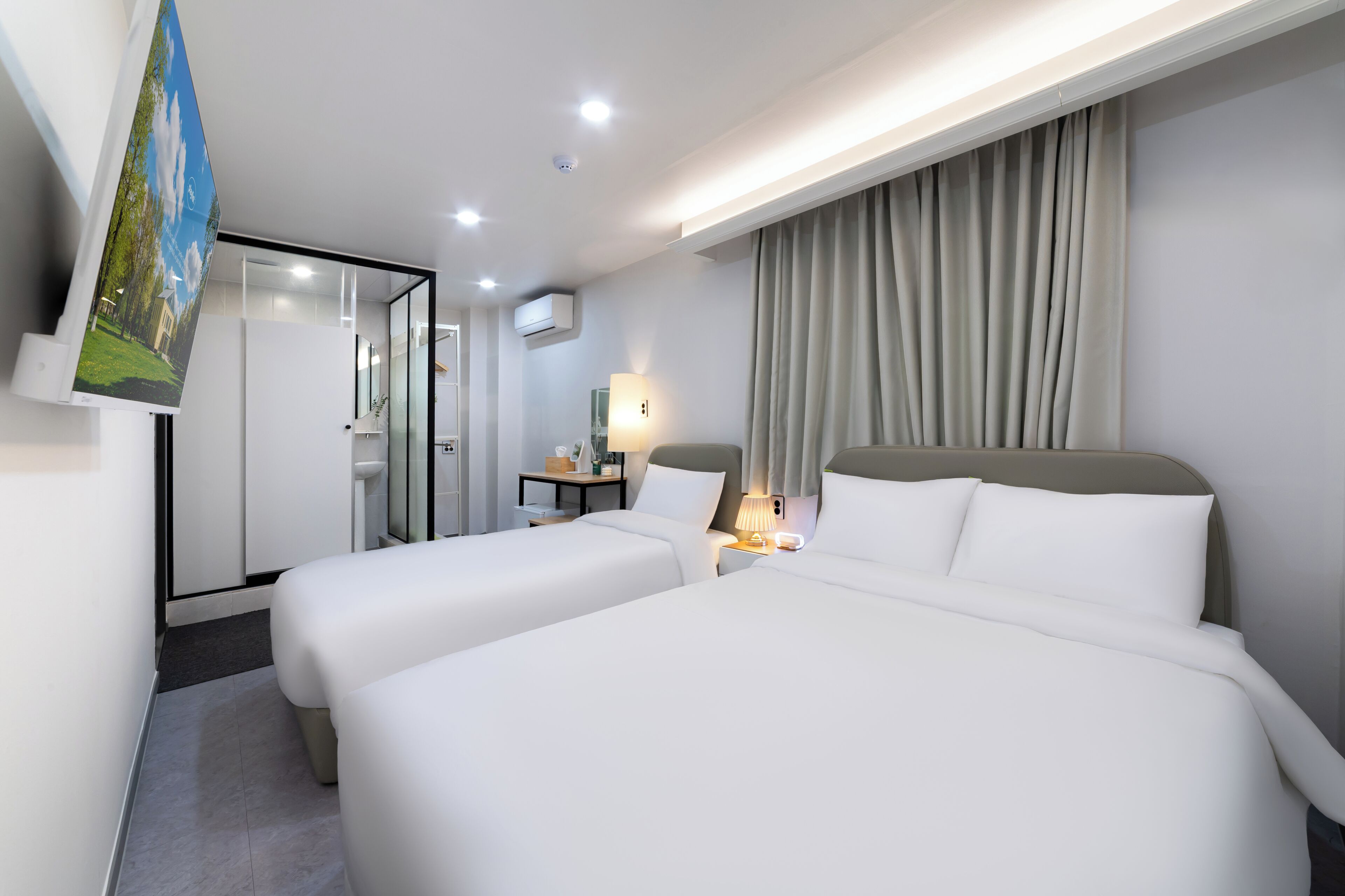 Ett hotellrum med två sängar, ett skrivbord, en lampa och utsikt över en byggnad genom en glasdörr.