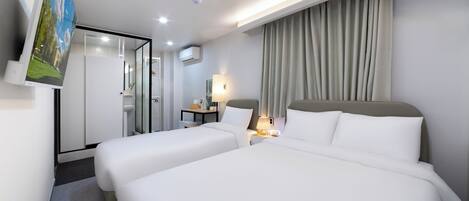 Habitación de hotel con dos camas, un escritorio, una lámpara y vista a un edificio a través de un ventanal.