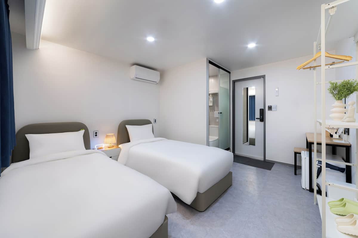 Una habitación de hotel moderna con dos camas, un escritorio, una silla, una planta colgante y un espejo.
