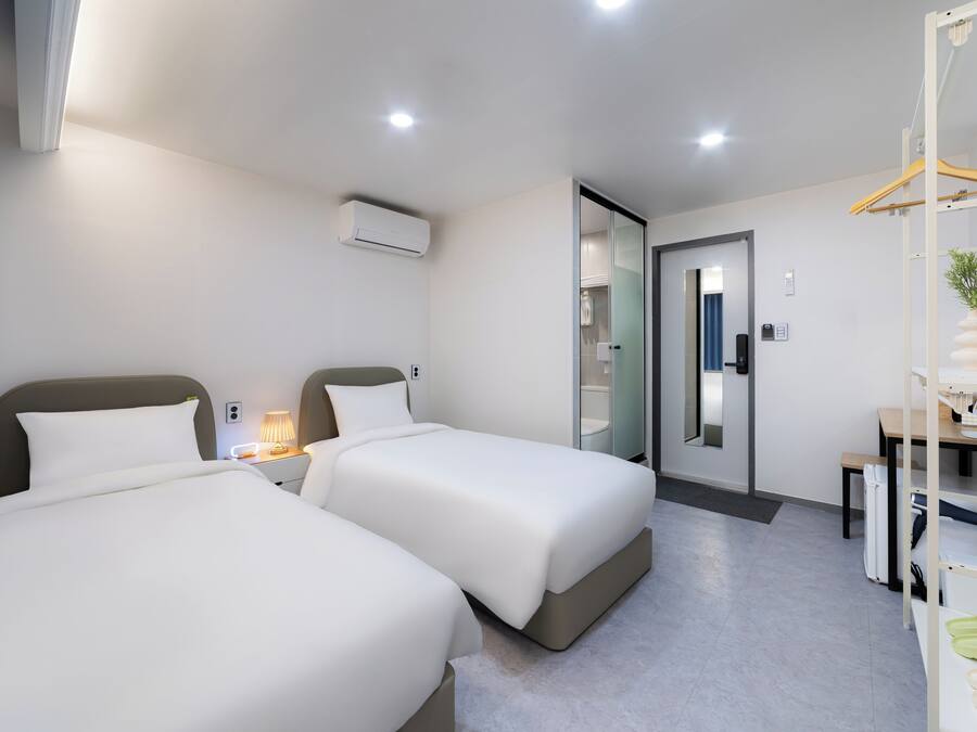 Una habitación de hotel moderna con dos camas, un escritorio, una silla, una planta colgante y un espejo.