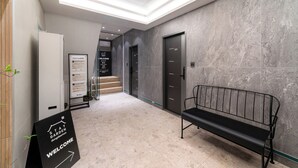 A modern hotel lobby with a reception desk, a signboard, a bench, and a staircase leading to an elevator. - Dongdaemun Stay Garden (Seoul)