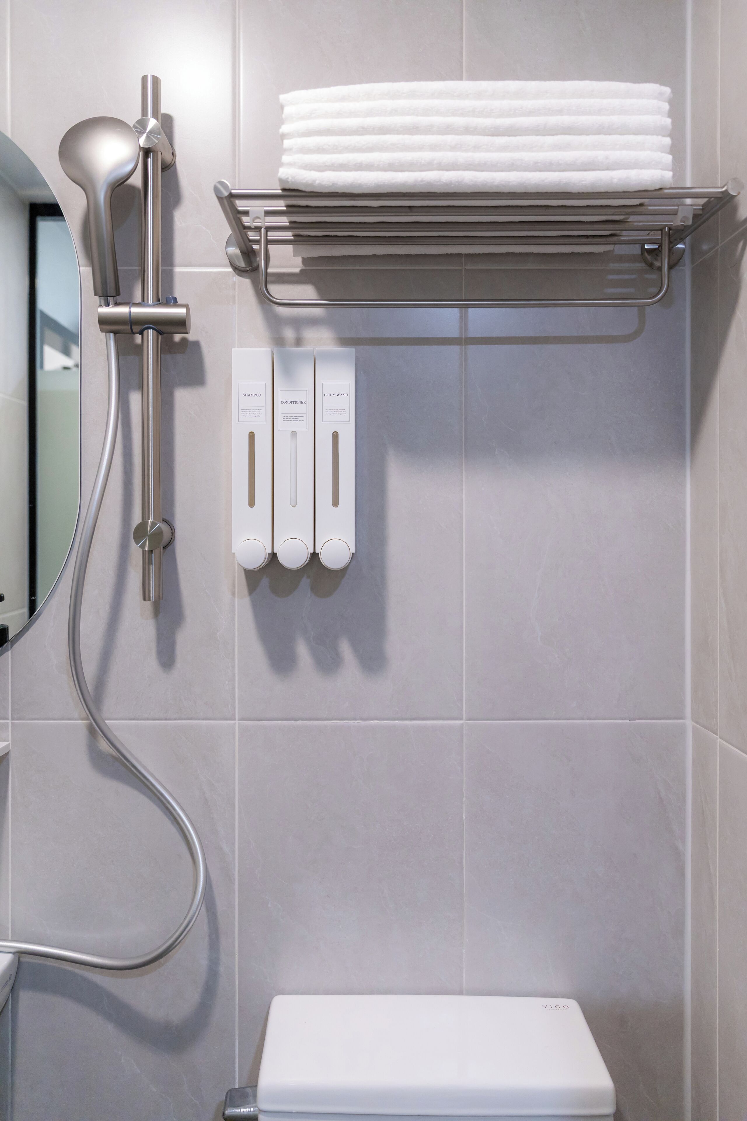 A bathroom with a toilet, a towel rack with folded towels, a shower control panel, and a hand dryer.