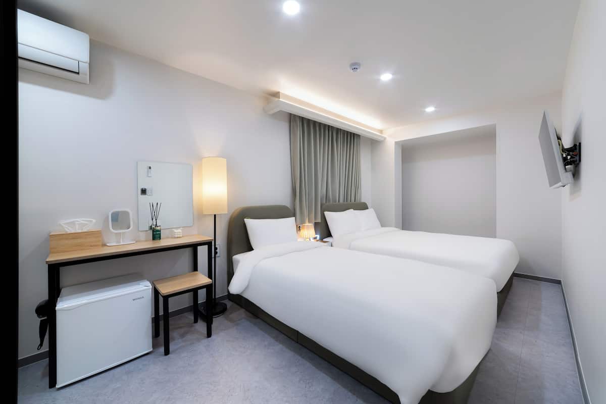 Habitación de hotel con una cama, un escritorio con ordenador, un mini refrigerador, una lámpara y un televisor fijado a la pared.