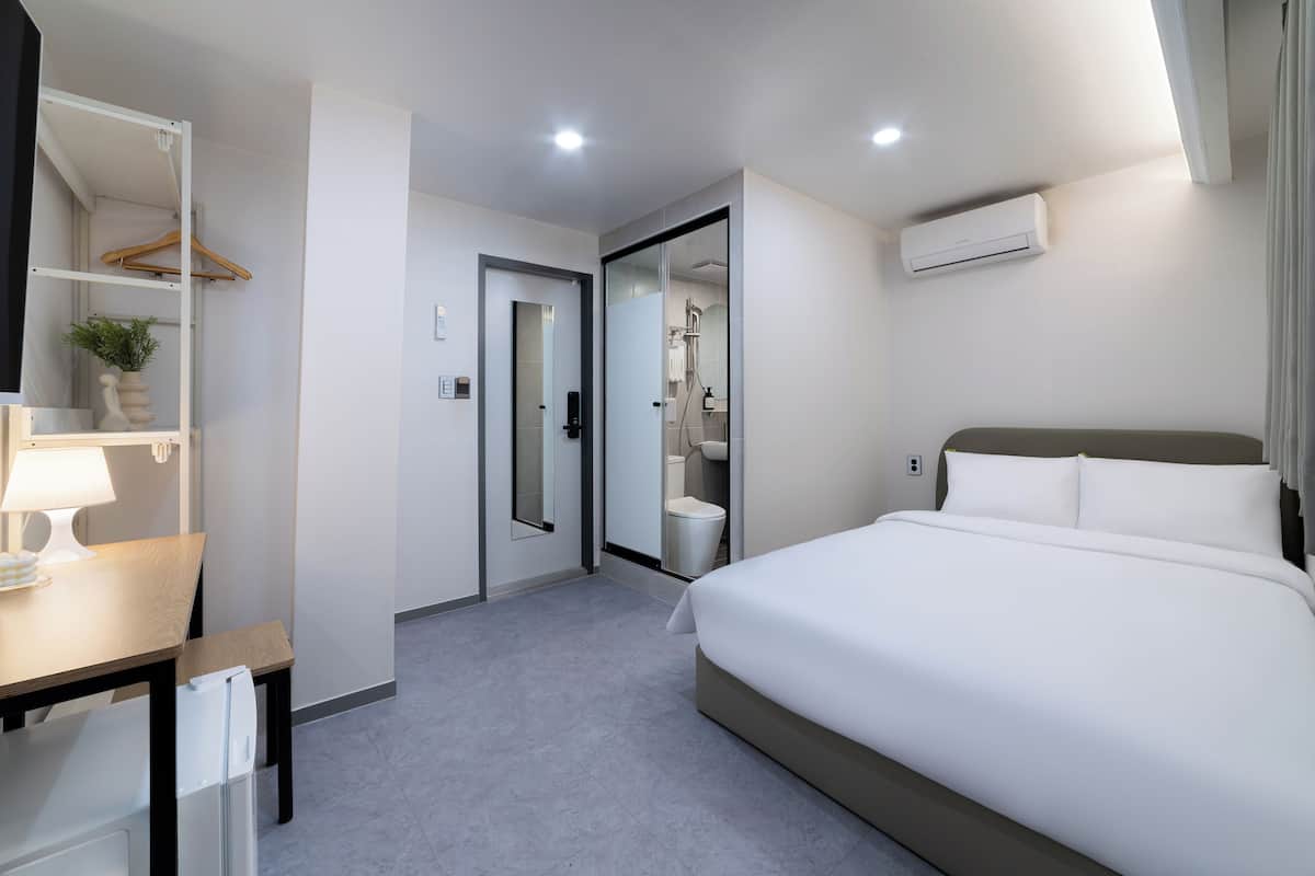 Habitación de hotel moderna con una cama, un escritorio con lámpara, un armario y un equipo de aire acondicionado.