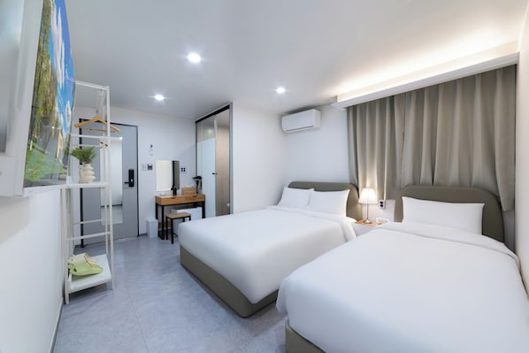 Hotelkamer met twee bedden, een bureau, een stoel, een plank met een plant en een airconditioner.