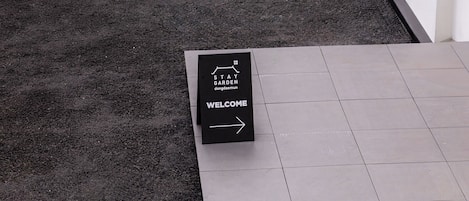 A welcome sign in a courtyard with a wall mural and a building entrance.