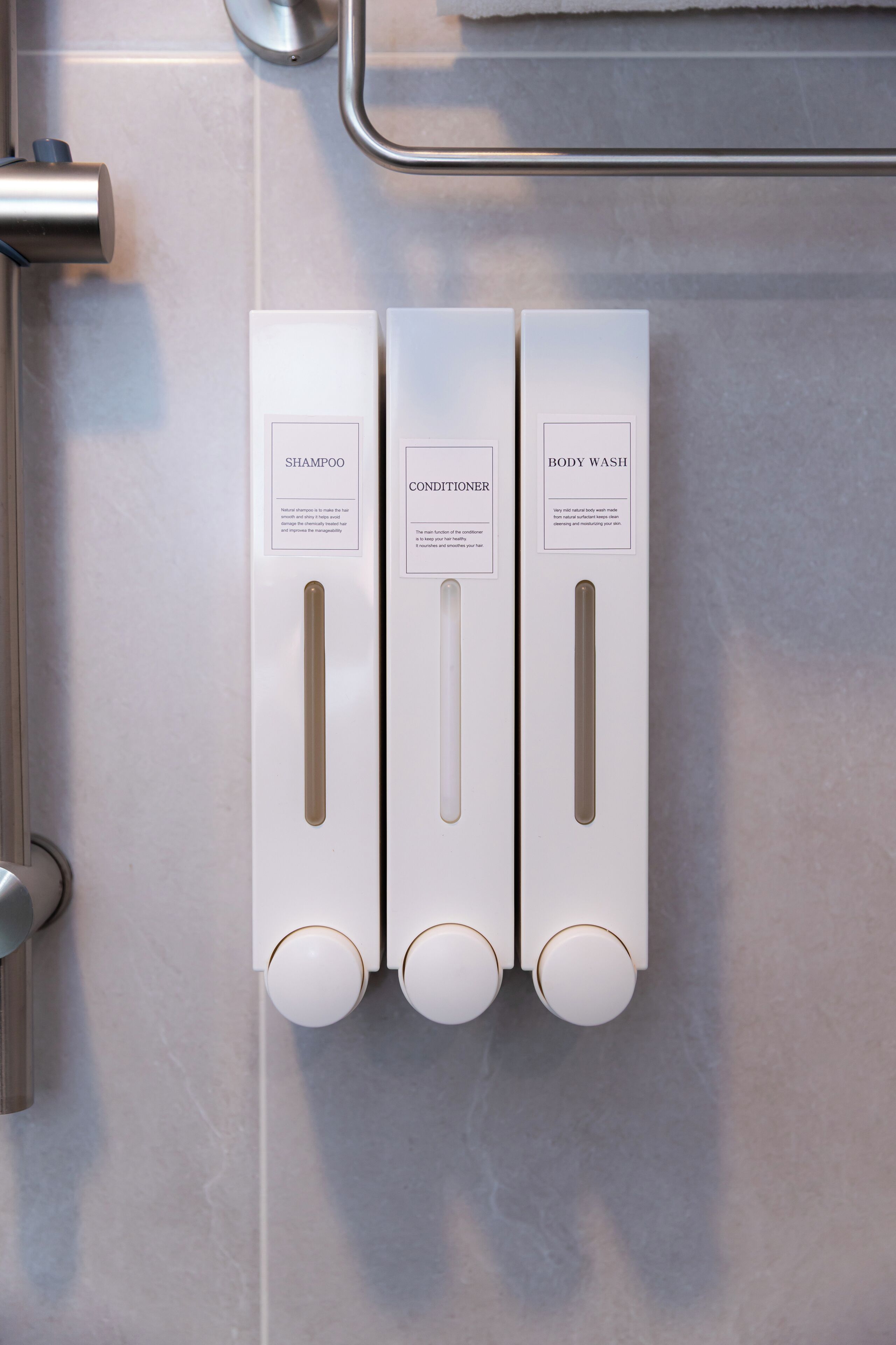 A bathroom with three dispensers labeled 'SHAMPOO,' 'CONDITIONER,' and 'BODY WASH.'