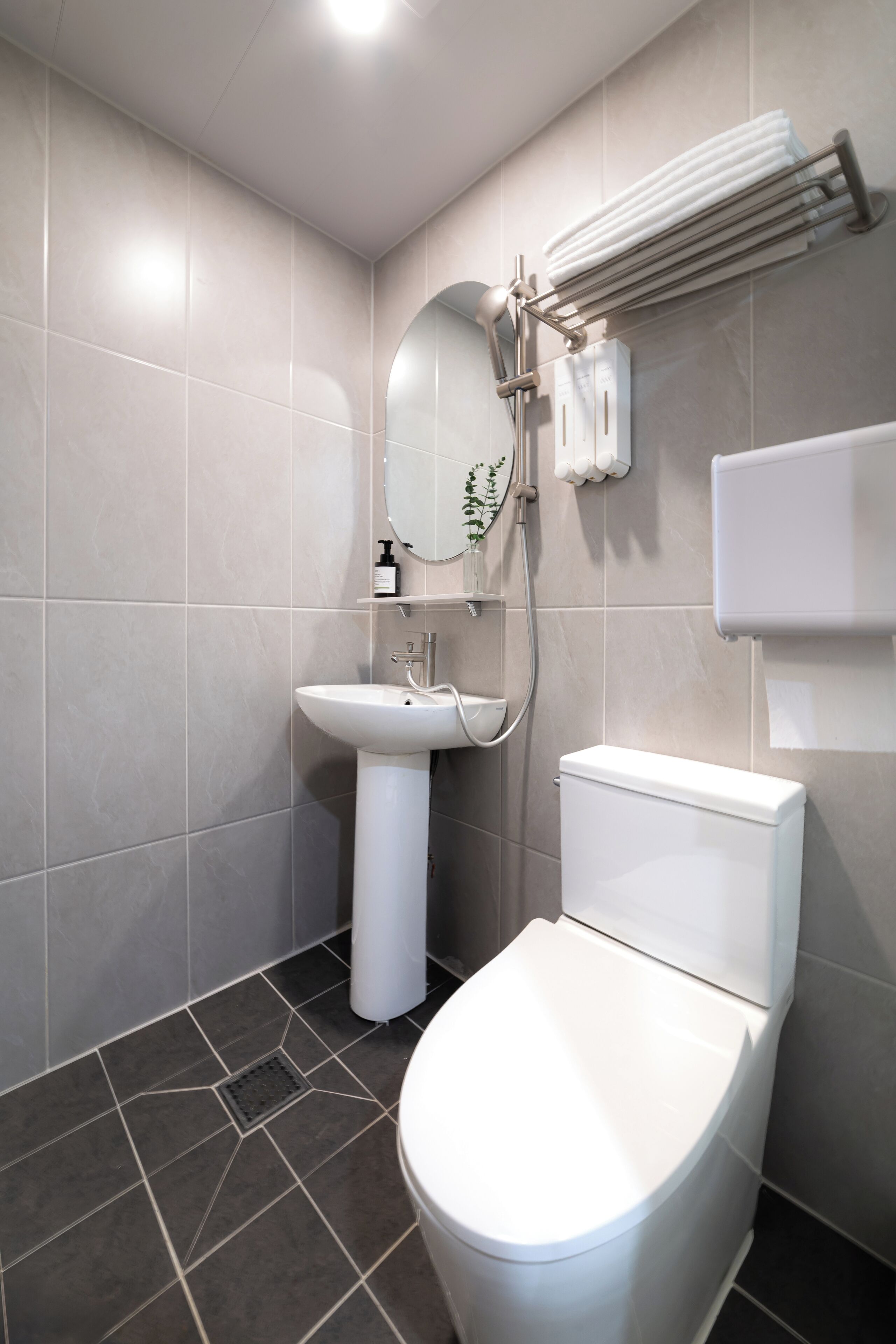 A modern bathroom with a white toilet, pedestal sink, and a towel rack.