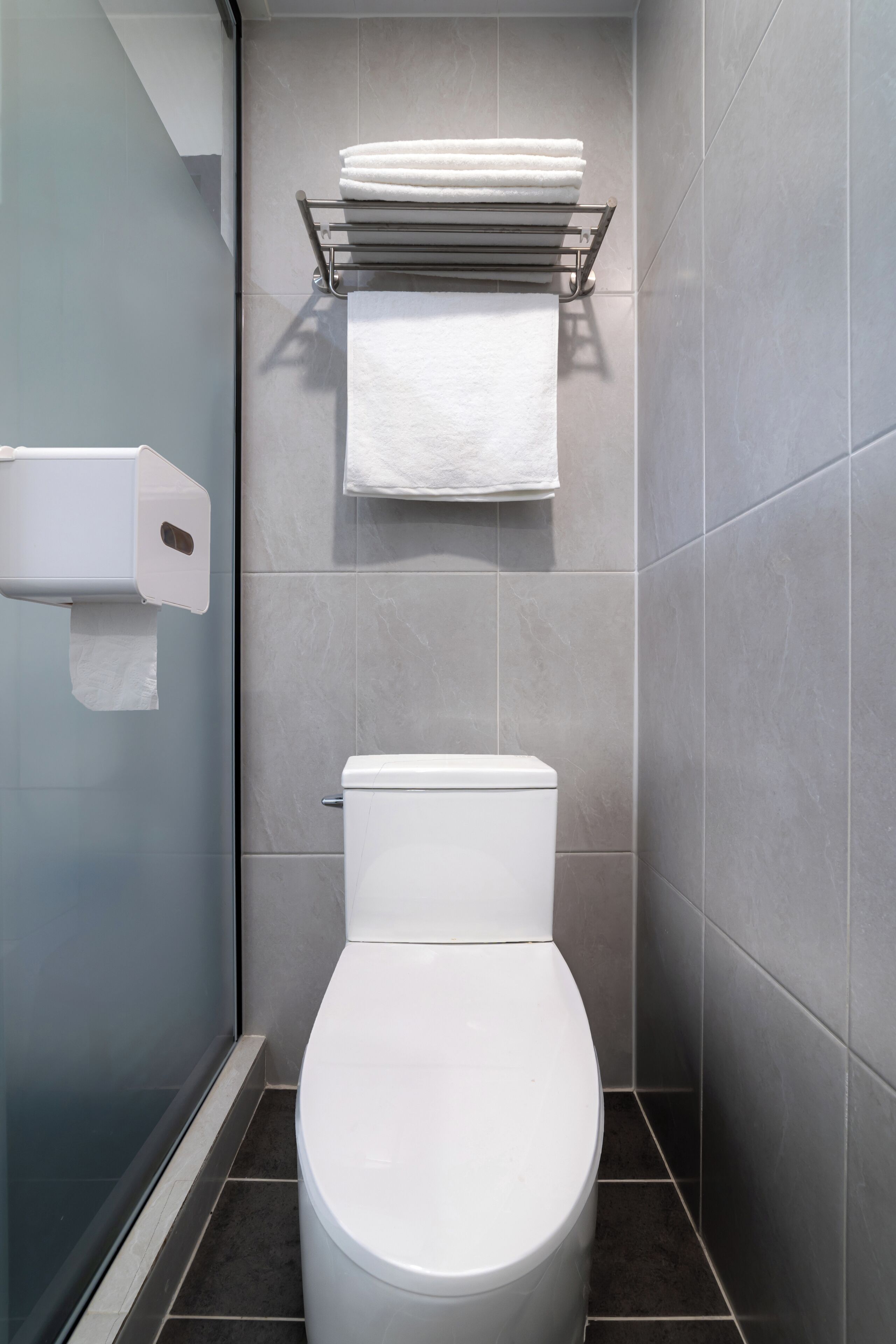 A modern bathroom with a toilet, a towel rack with folded towels, and a paper towel dispenser.