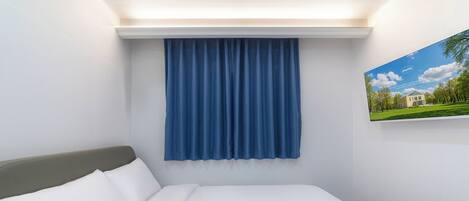 Una habitación de hotel con una cama, una cortina azul y un cuadro en la pared.