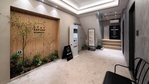 A modern hotel lobby with a reception desk, a welcome sign, a staircase, and a wall-mounted plant. - Dongdaemun Stay Garden (Seoul)