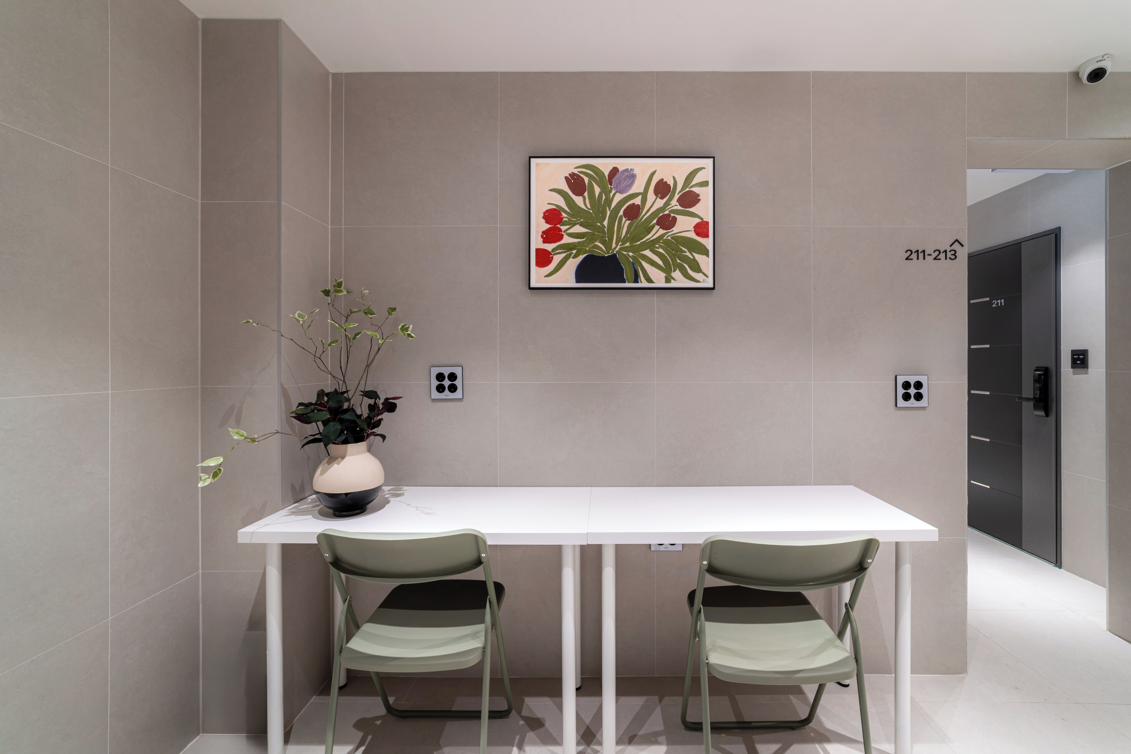 A modern room with a white table, two chairs, a potted plant, and a framed floral artwork on the wall.